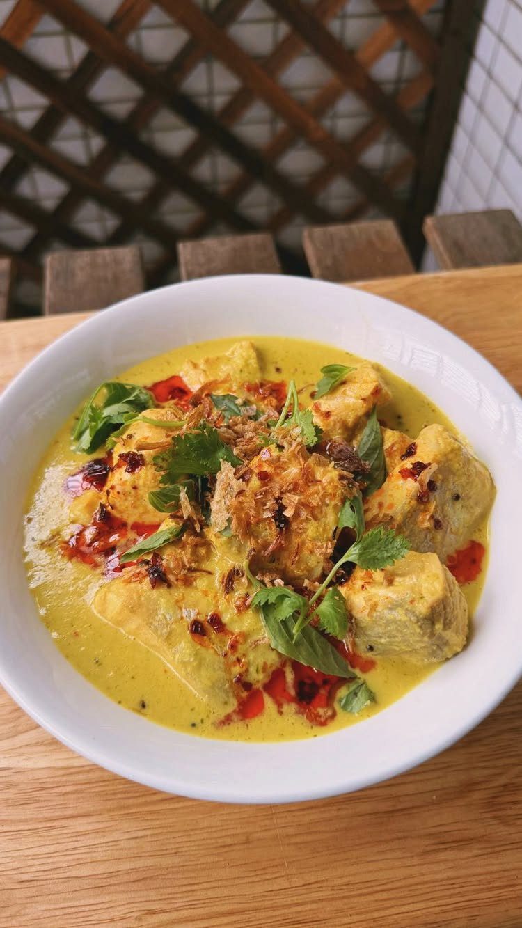 Yellow coconut fish curry with cilantro and fried shallots in a white bowl.