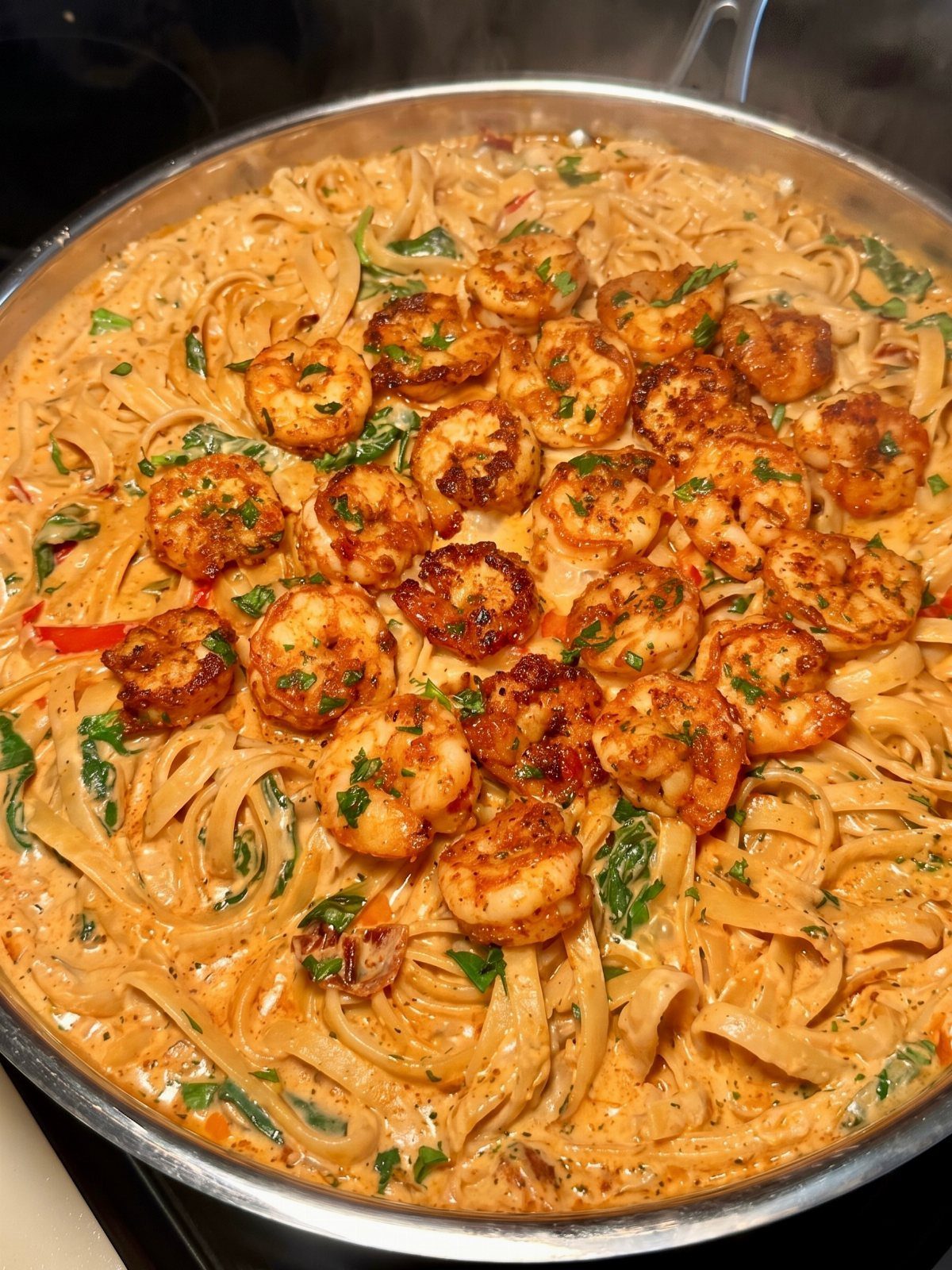 Creamy orange pasta topped with seared seasoned shrimp in a stainless steel skillet.