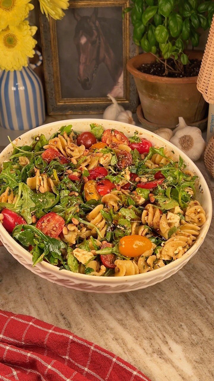 Rotini pasta with green pesto, cherry tomatoes, and spinach in a white bowl.