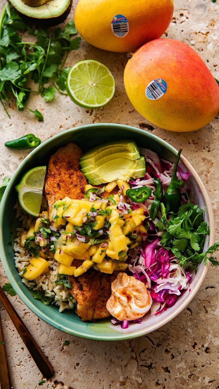 Grilled fish fillets topped with mango salsa in a bowl with avocado and slaw.