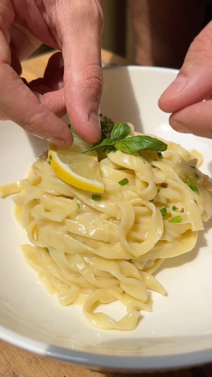 Creamy fettuccine pasta in a white bowl garnished with lemon and fresh basil.