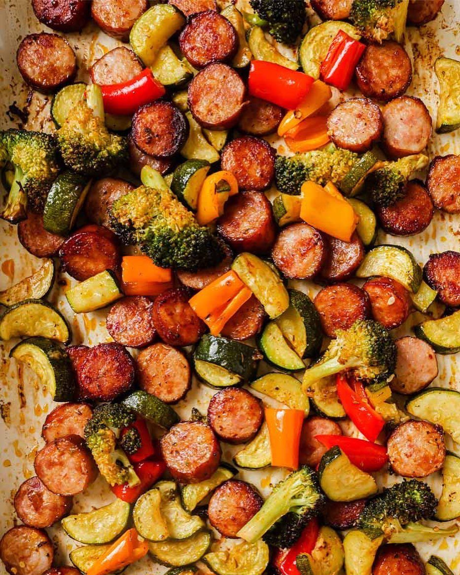 Roasted sliced sausages with broccoli, zucchini, and colorful bell peppers on a sheet pan.