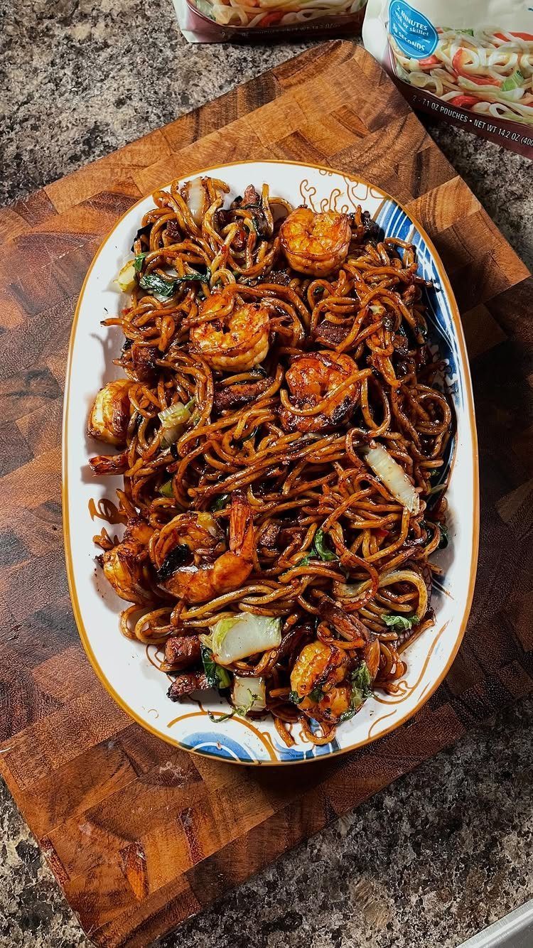 Stir-fried noodles with shrimp and cabbage on a white platter over wood.