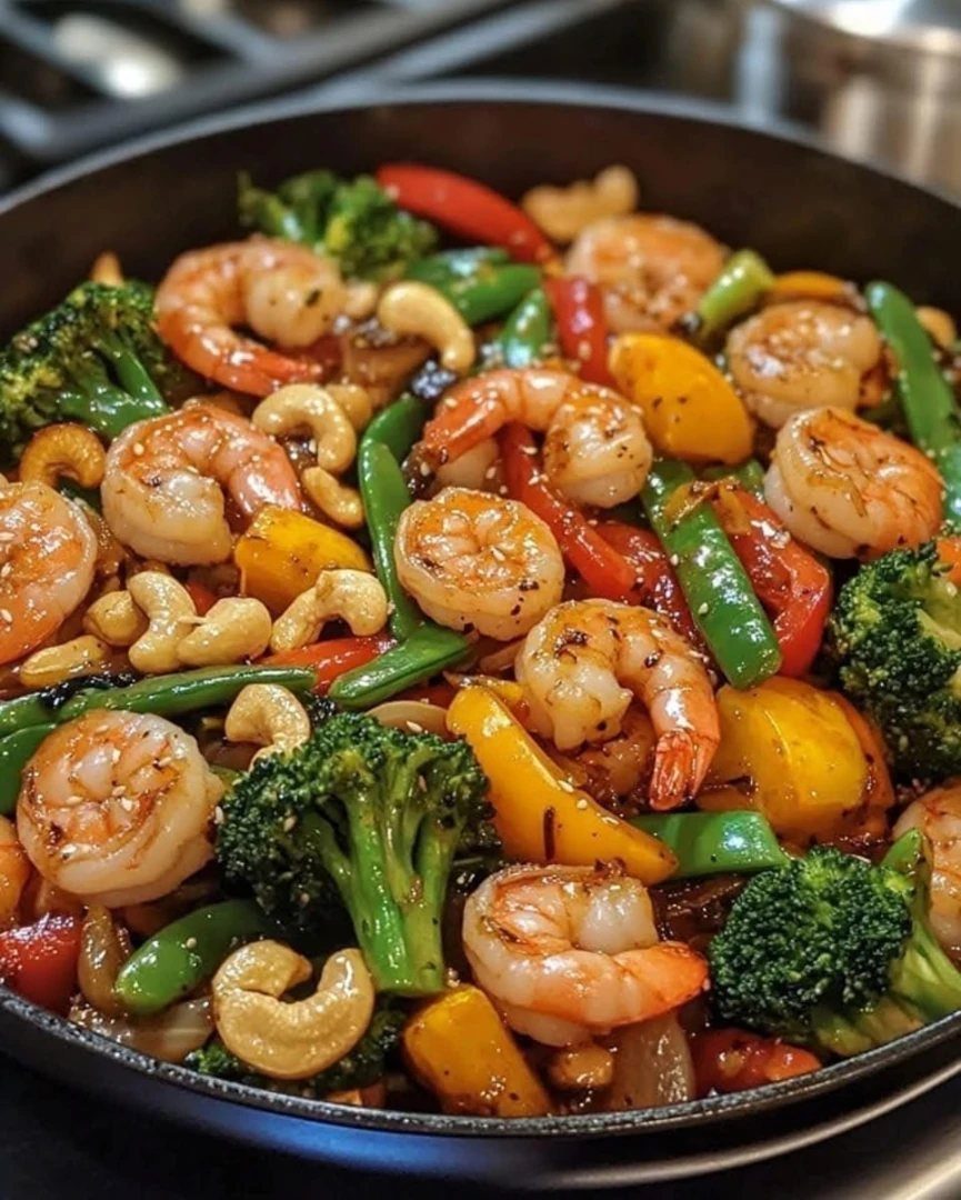 Shrimp stir-fry with broccoli, bell peppers, snap peas, and cashews in a skillet