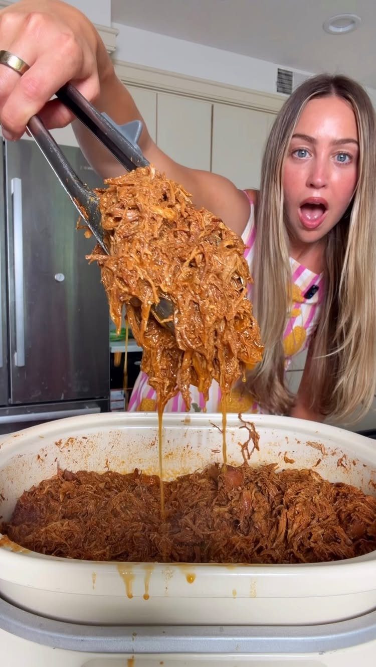Shredded BBQ chicken being lifted from a slow cooker by a woman.