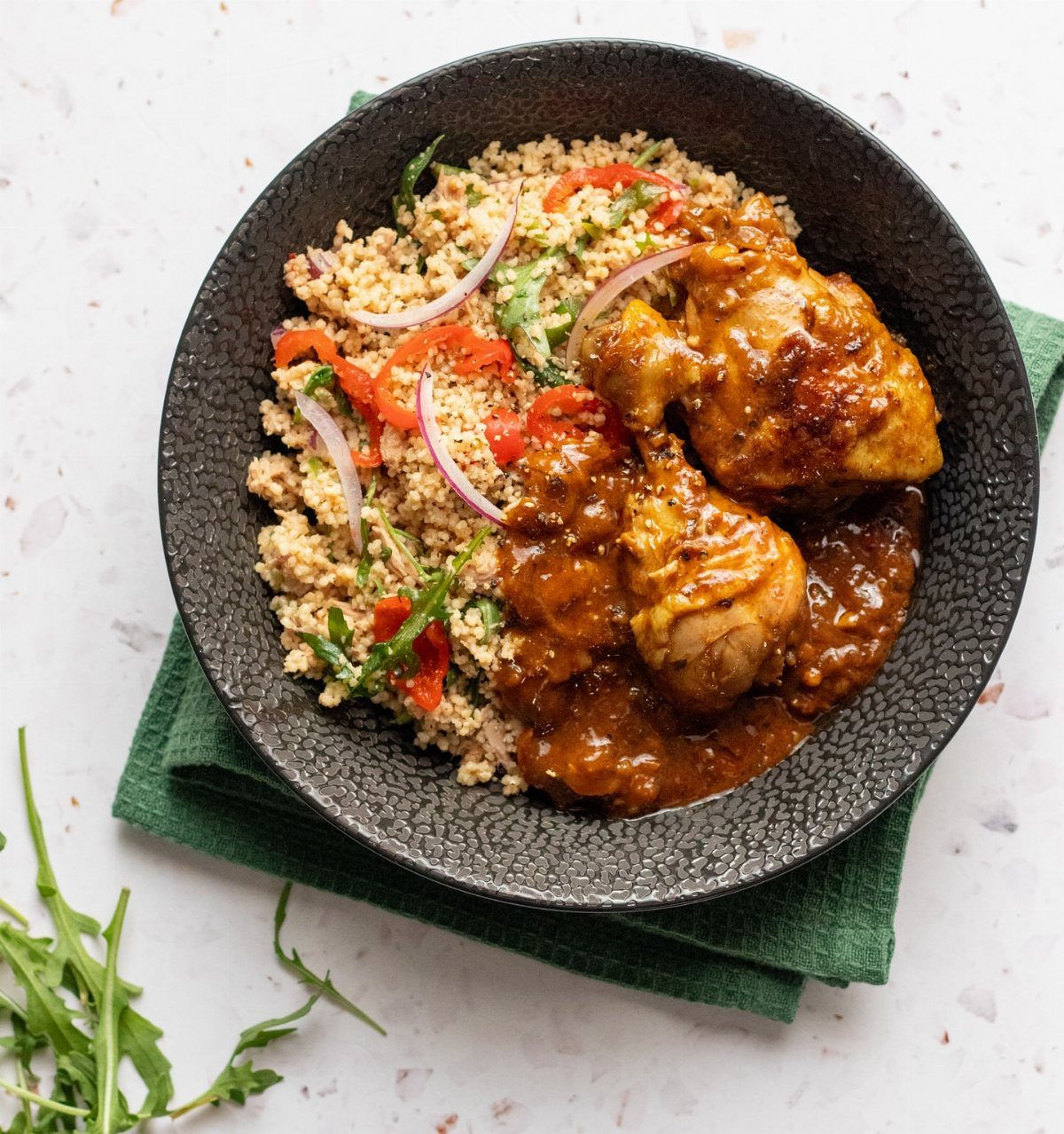 Chicken in brown sauce served with couscous and red peppers in a black bowl.