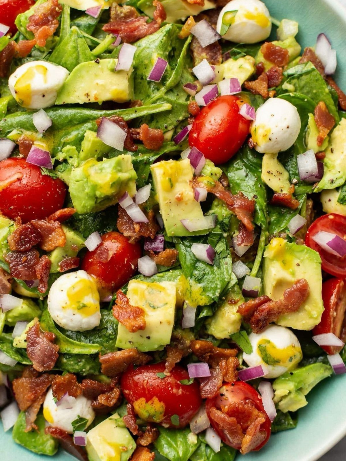 Spinach salad with cherry tomatoes, avocado, mozzarella, bacon, and red onion.