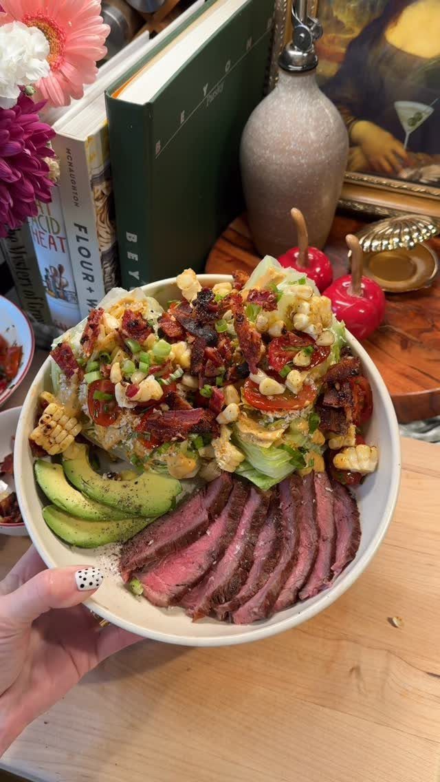 Sliced medium-rare steak and avocado with a corn and bacon salad in a bowl.