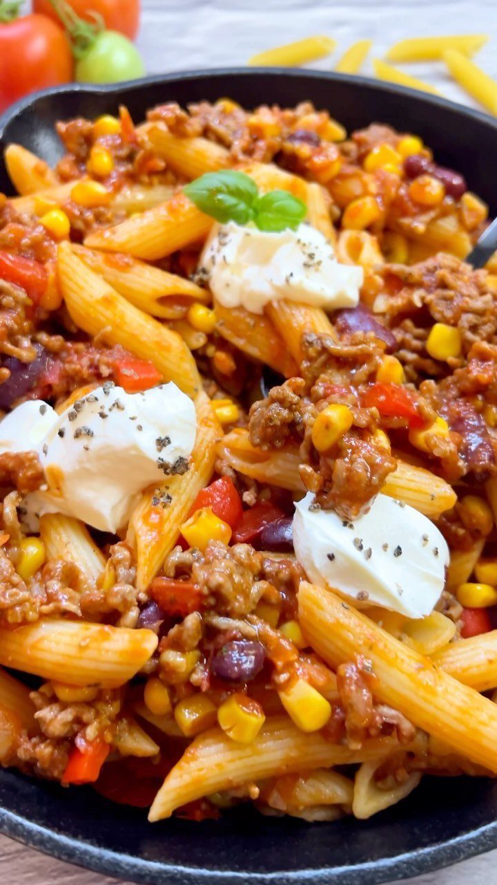 Penne pasta with ground meat, corn, and beans in a skillet topped with cream.