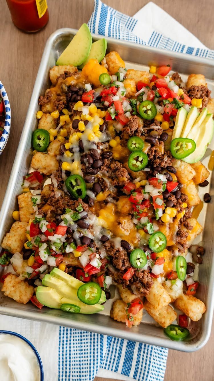 Tater tots topped with seasoned beef, melted cheese, beans, corn, and avocado slices.