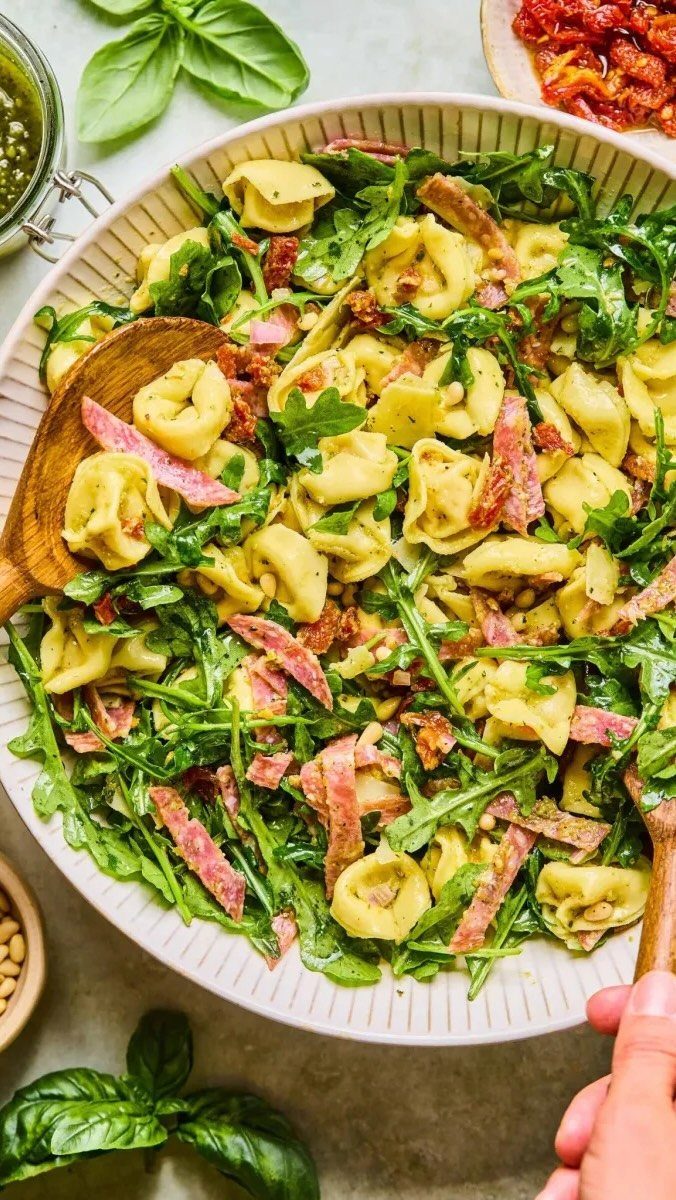 Tortellini pasta salad with arugula and salami in a white fluted bowl.