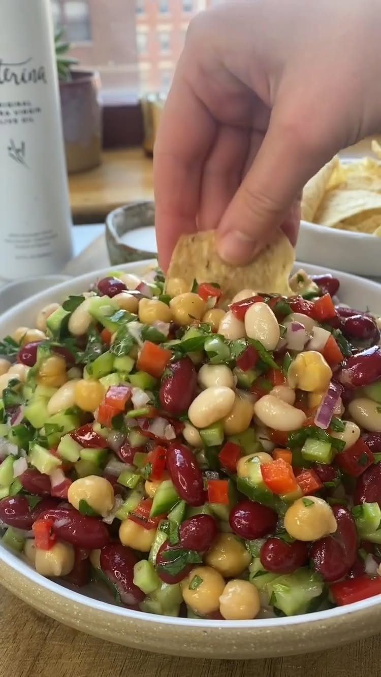 Bean salad with red and white beans, chickpeas, and vegetables with a chip.