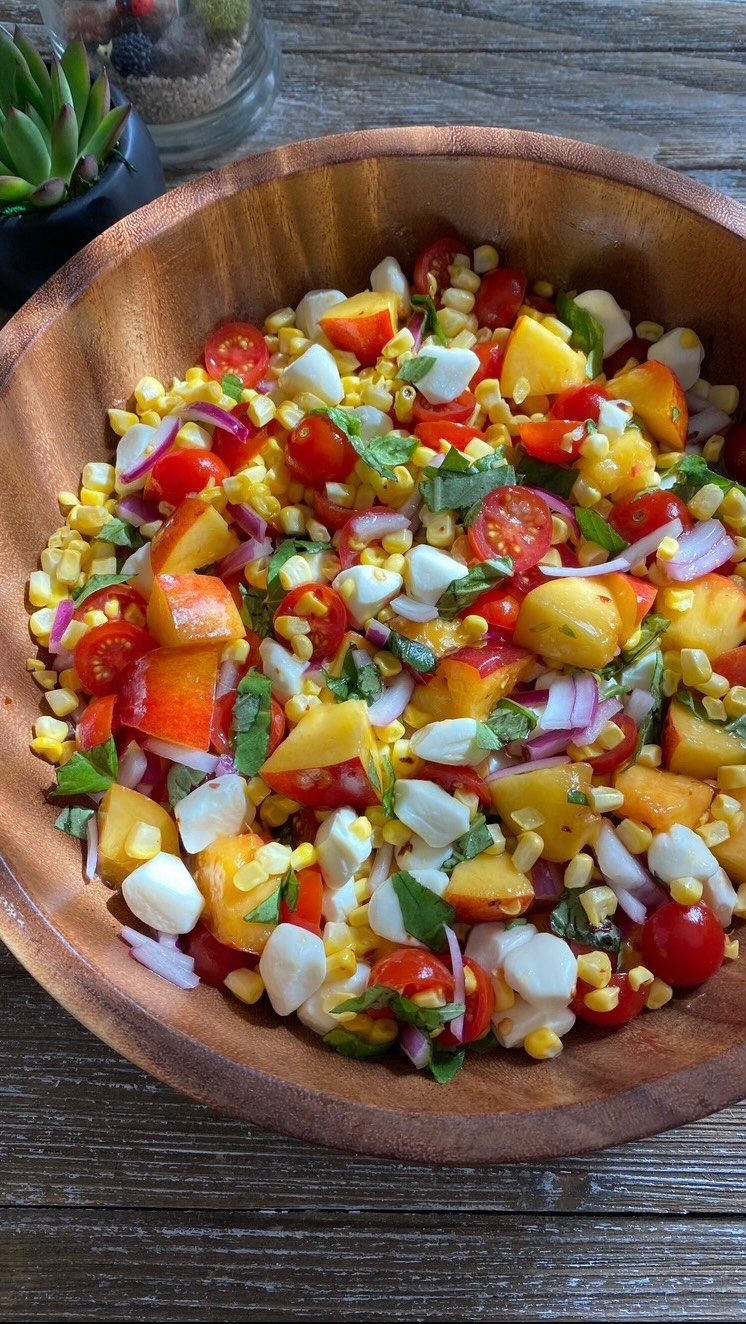 Corn and basil salad with tomatoes, mozzarella, and peaches in a wooden bowl.