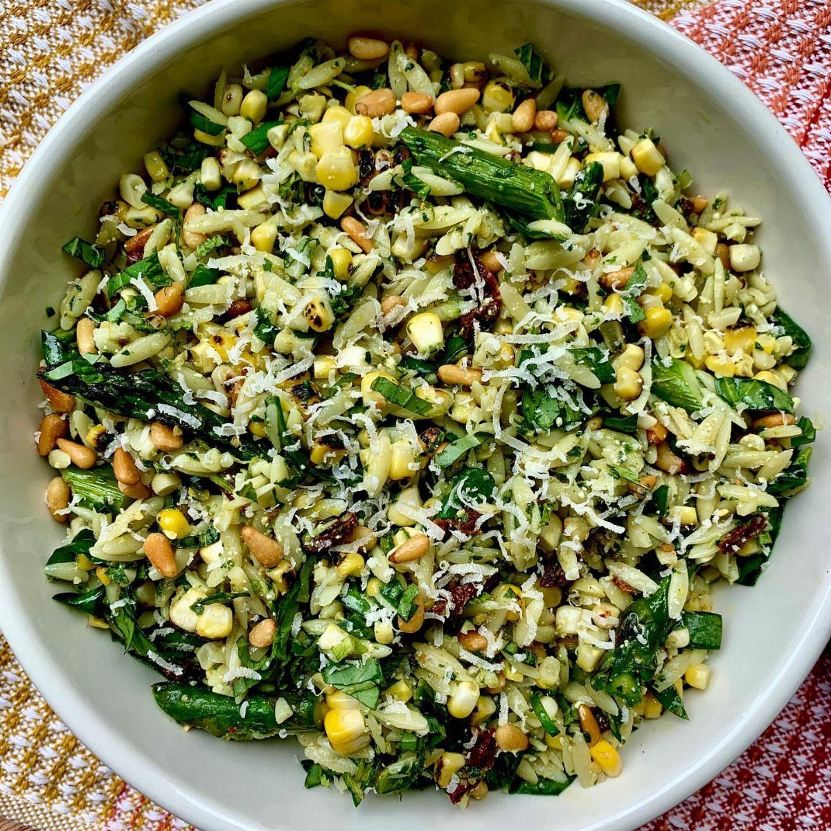 Orzo pasta salad with corn, asparagus, and pine nuts in a white bowl.
