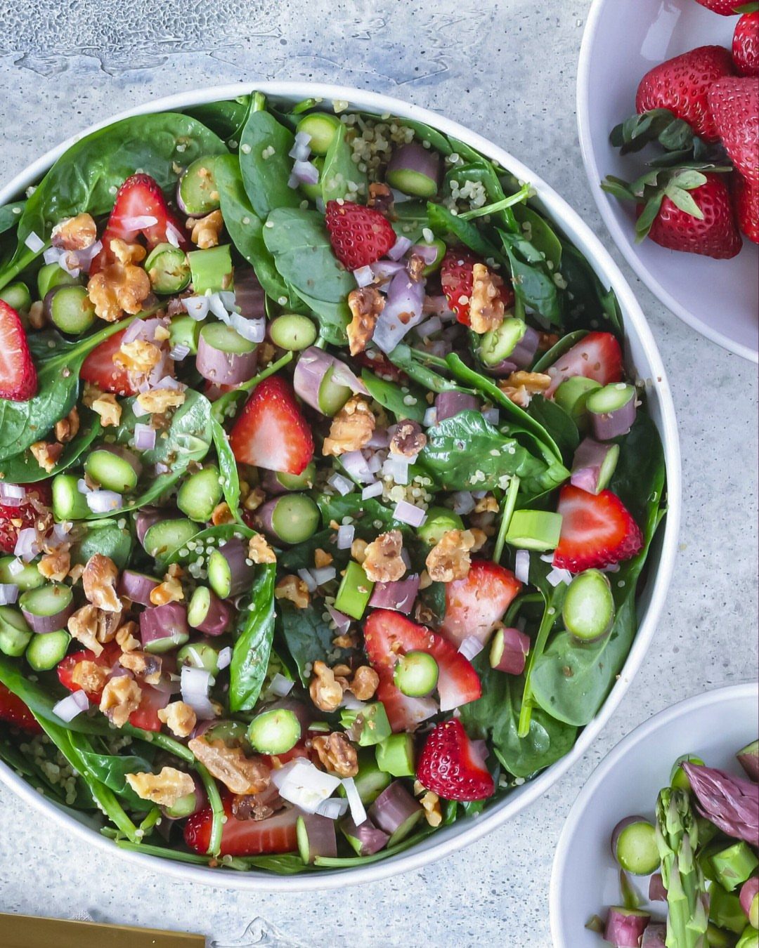 Strawberry quinoa salad with spinach, walnuts, and cucumbers in a white bowl.