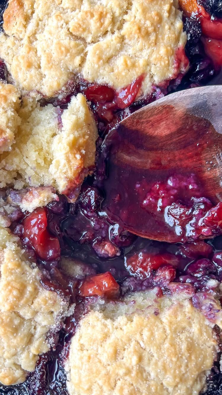 Blueberry peach cobbler with golden biscuit topping and a wooden serving spoon.