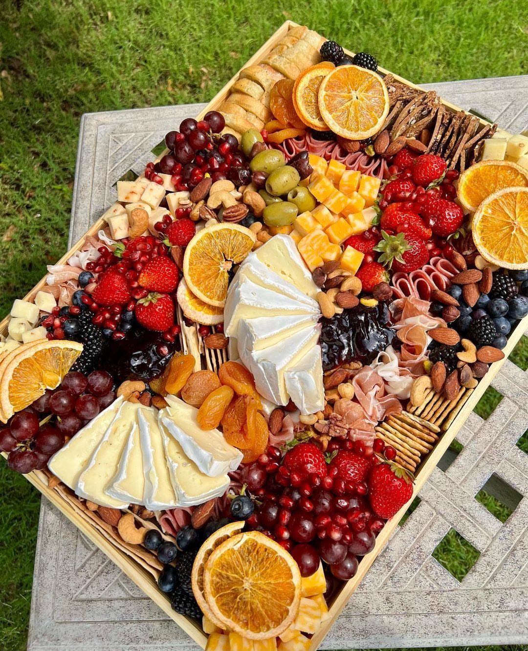 Charcuterie board with assorted cheeses, meats, fresh berries, grapes, and dried citrus slices.