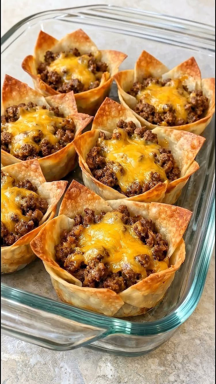 Tortilla cups filled with seasoned ground beef and melted cheese in glass dish