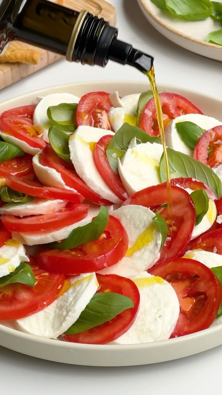 Caprese salad with tomato, mozzarella, and basil being drizzled with olive oil.