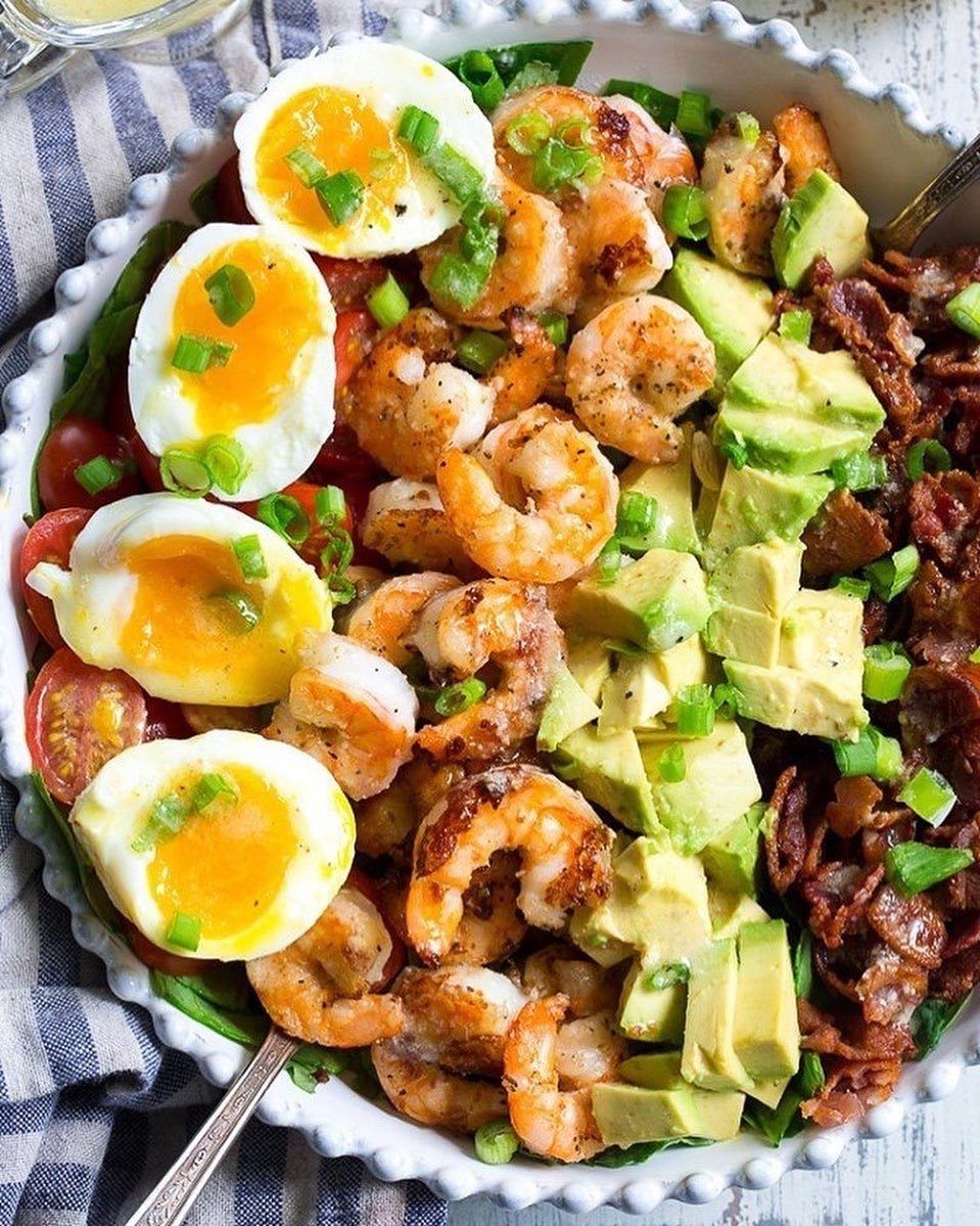 Salad bowl with soft-boiled eggs, grilled shrimp, avocado, and bacon on spinach.