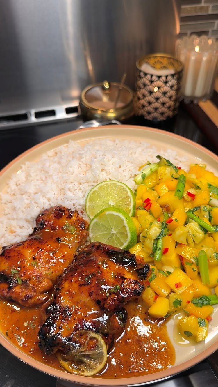 Glazed grilled chicken thighs served with white rice, mango salsa, and lime slices.