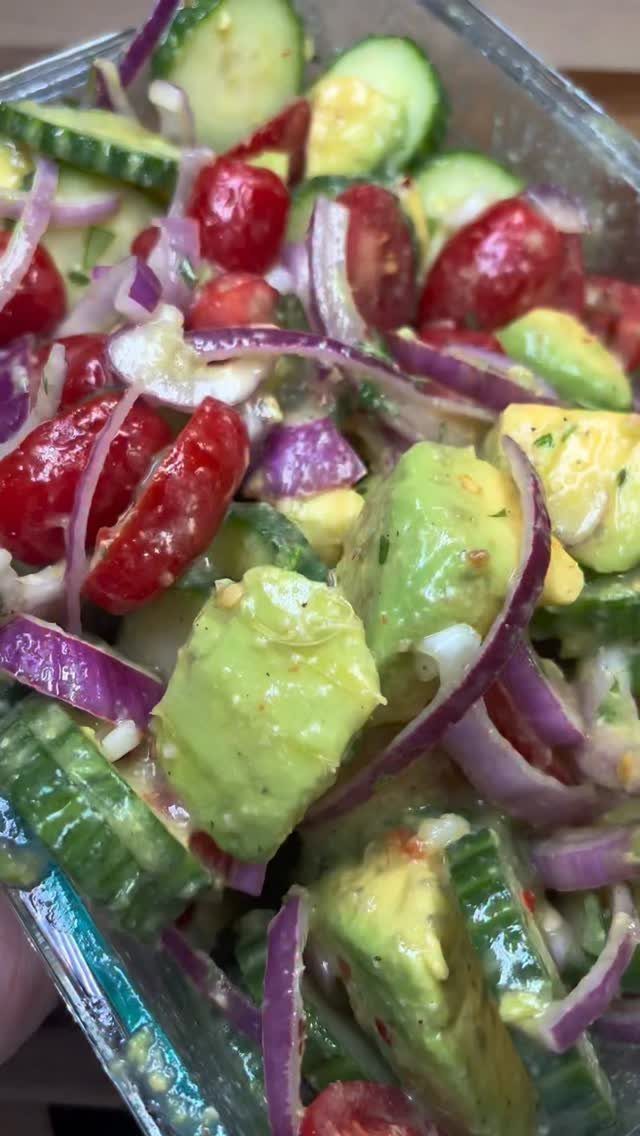 Fresh salad with cucumbers, avocado, cherry tomatoes, and red onion in glass container.