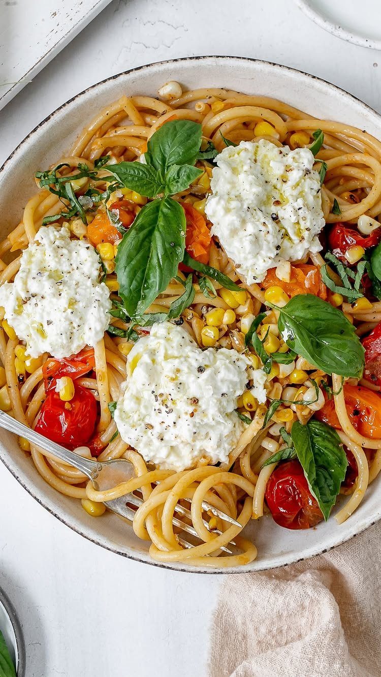 Pasta with corn, cherry tomatoes, ricotta cheese, and fresh basil in a bowl.