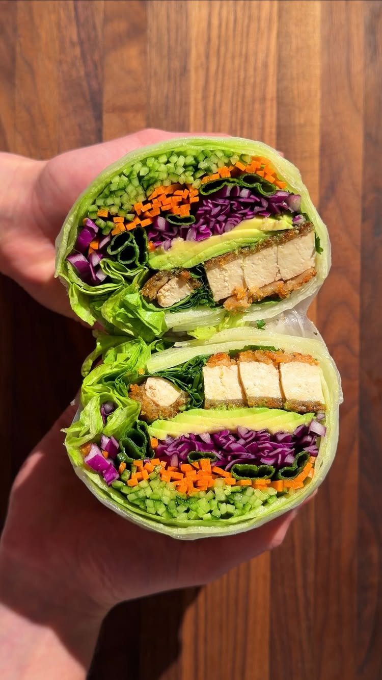 Green tortilla wrap halves filled with tofu, avocado, and colorful shredded vegetables.