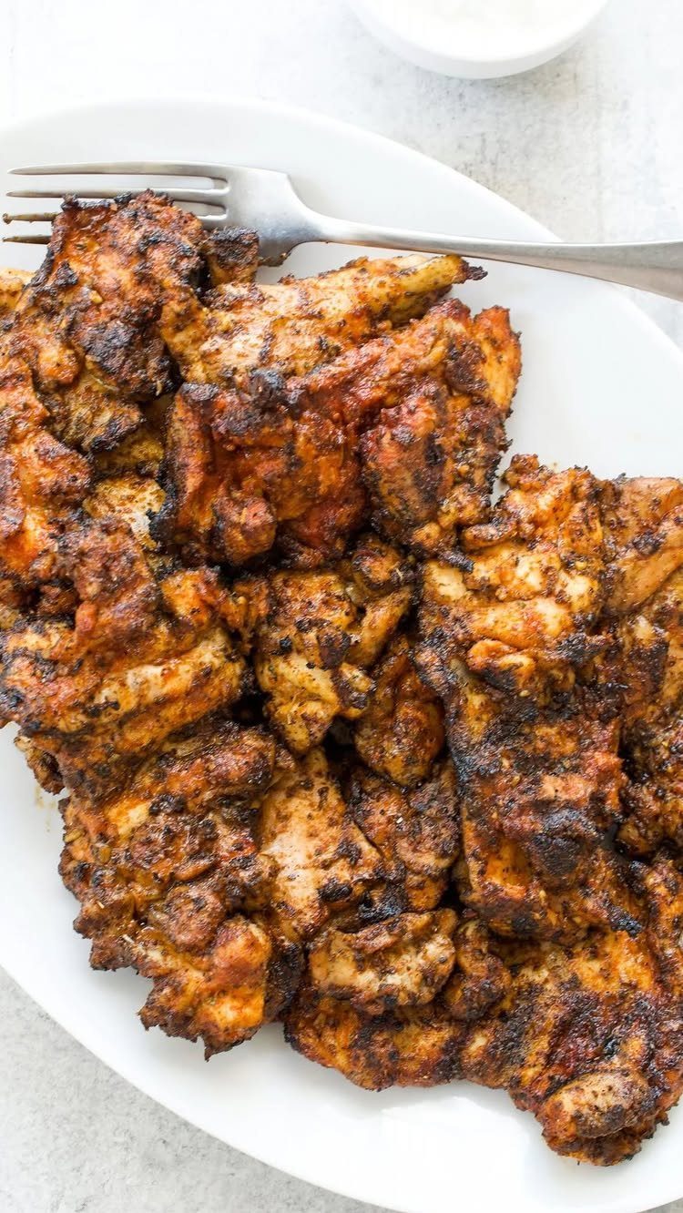 Seasoned grilled chicken pieces served on a white plate with a silver fork.