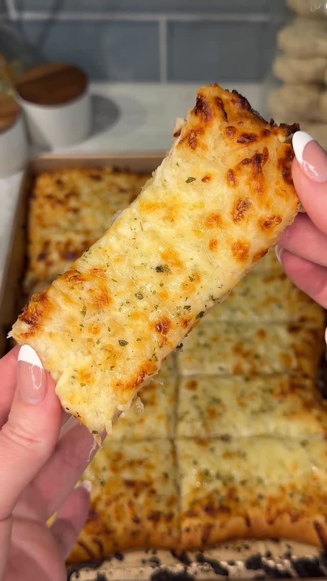 Cheesy garlic butter pizza slice held up over a baking tray.
