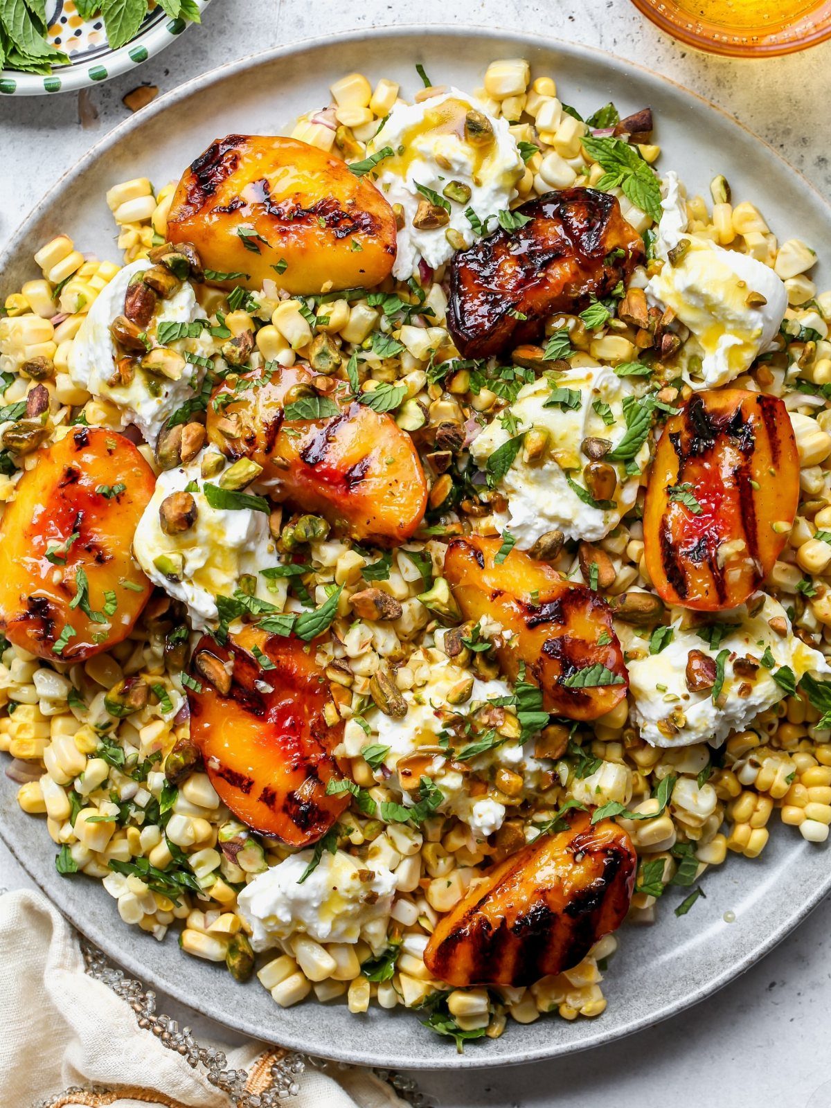 Grilled peach salad with corn, creamy cheese, and fresh herbs on a plate.