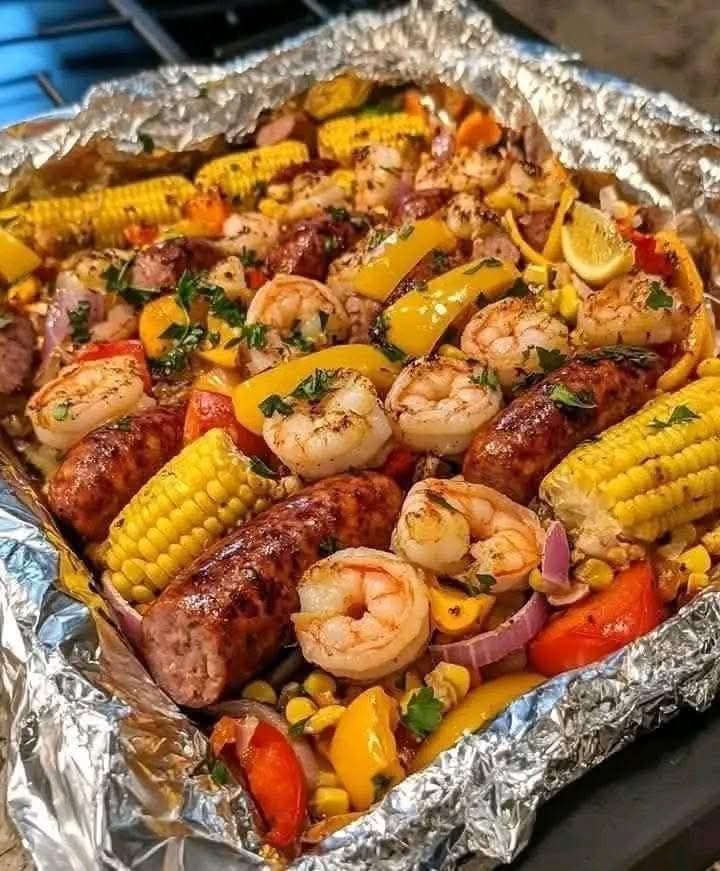 Grilled shrimp, sausages, corn, and peppers cooked in an aluminum foil packet.