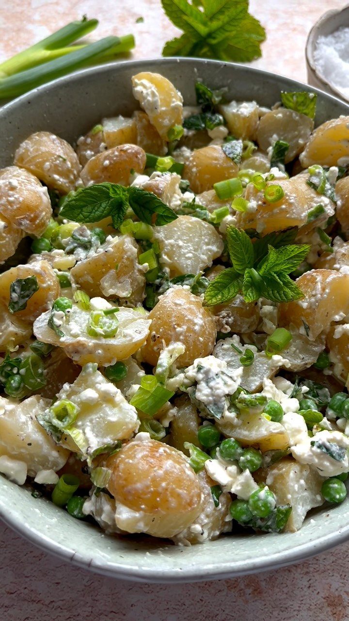 Creamy potato salad with peas, scallions, and mint leaves in a grey bowl.