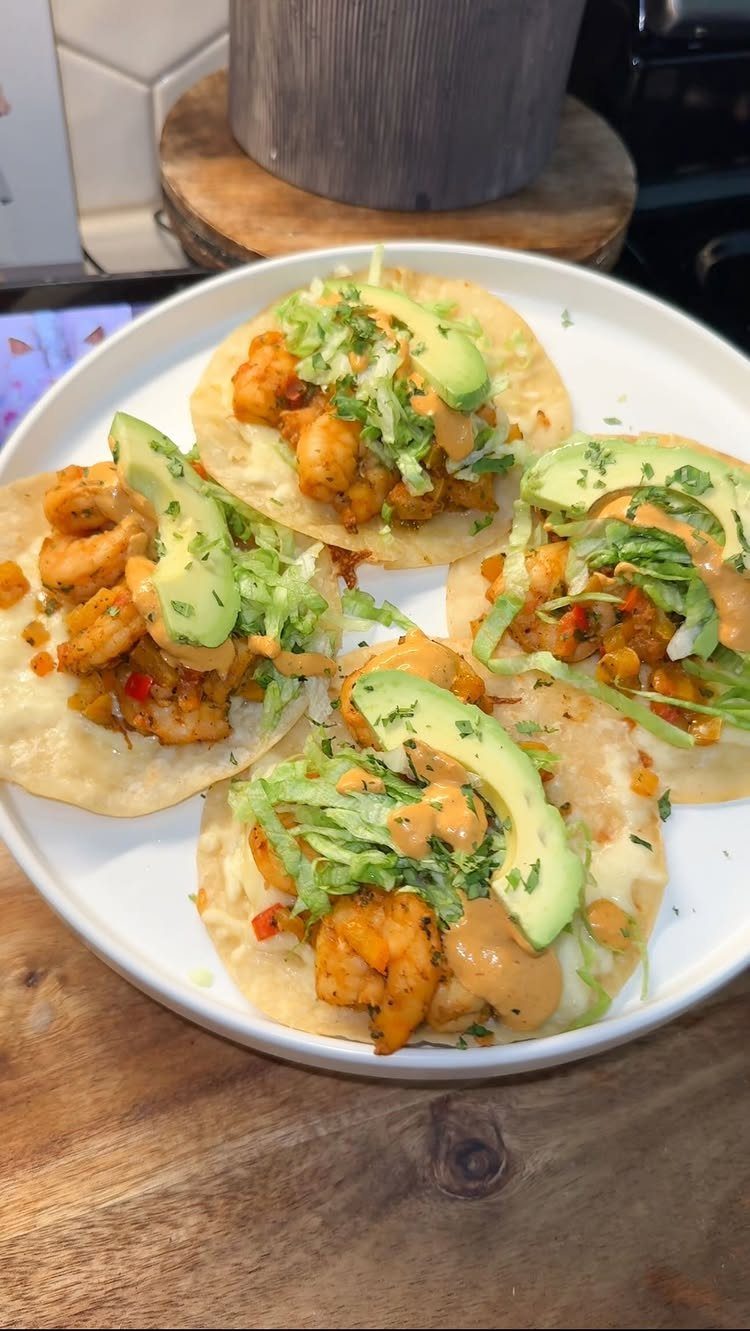 Shrimp tacos with avocado, lettuce, and creamy sauce on a white plate.