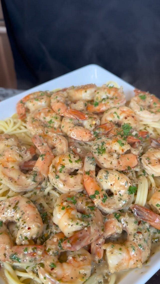 Garlic butter shrimp with parsley served over pasta in a white dish.