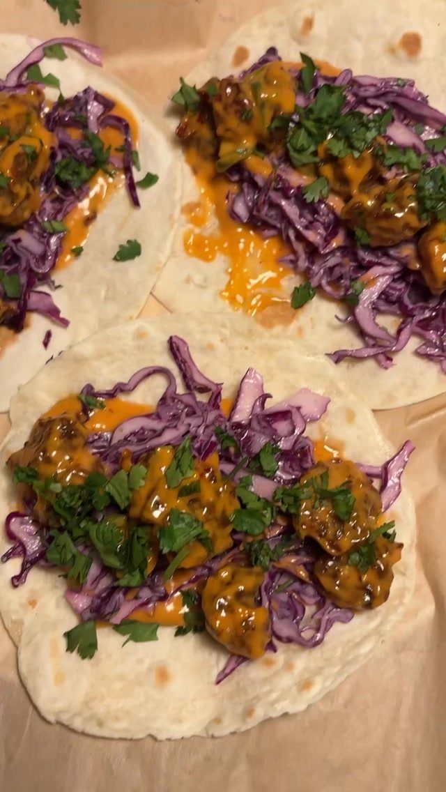 Shrimp tacos with purple cabbage, orange sauce, and cilantro on parchment paper.