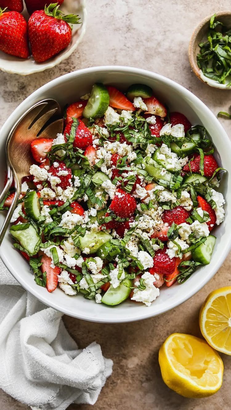 Strawberry and cucumber salad with feta cheese and herbs in a white bowl.
