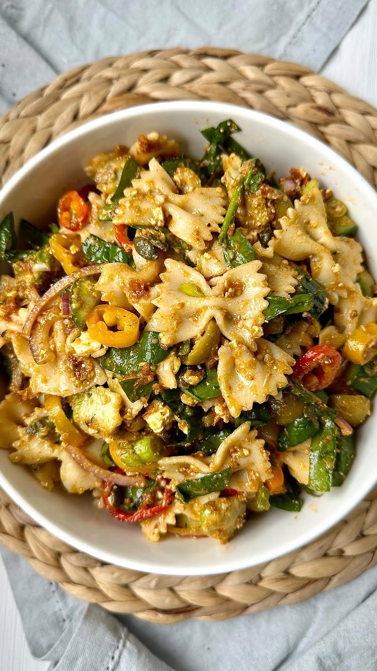 Farfalle pasta salad with mixed vegetables in a white bowl on a woven mat.