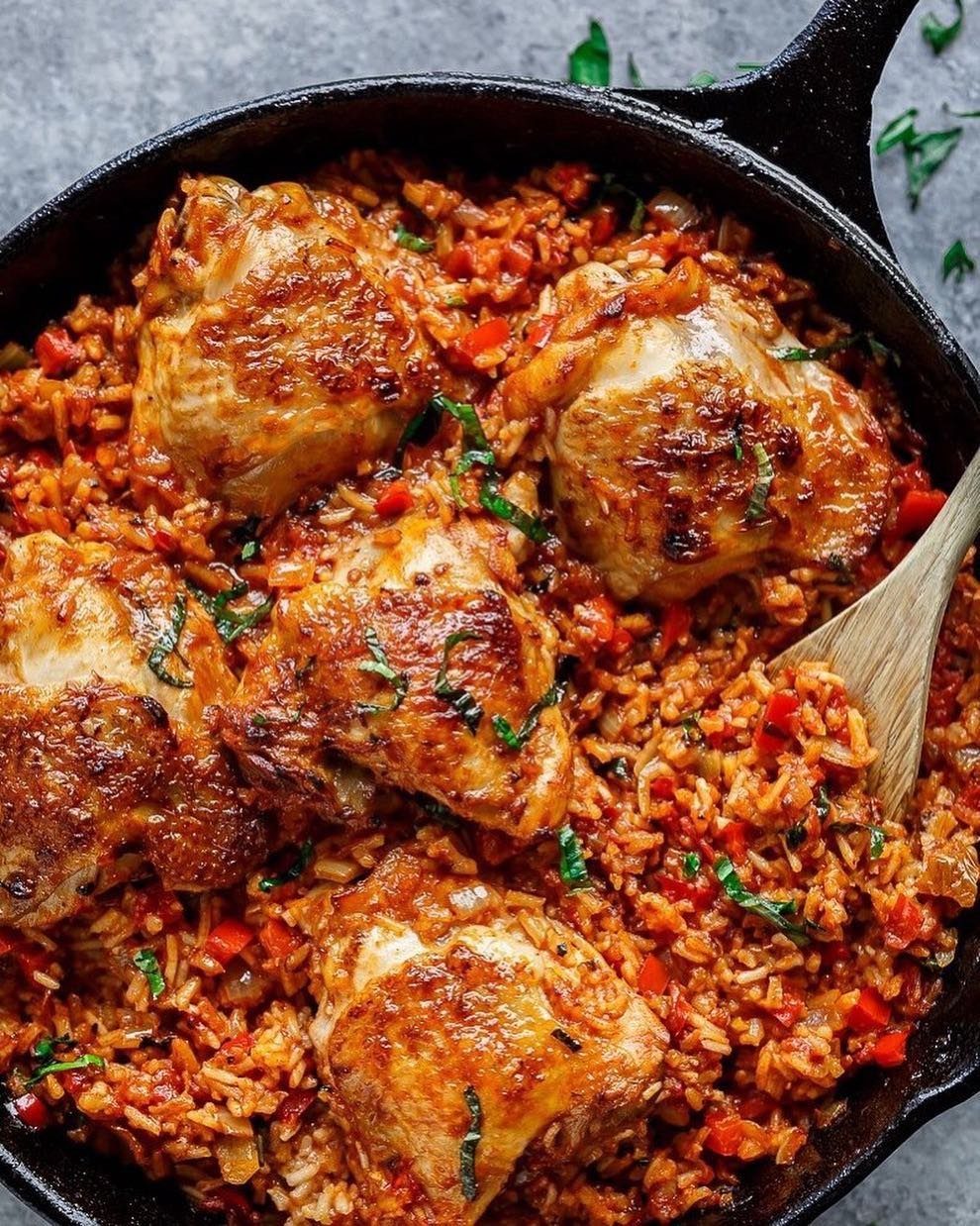 Browned chicken thighs and red rice with basil in a cast iron skillet.