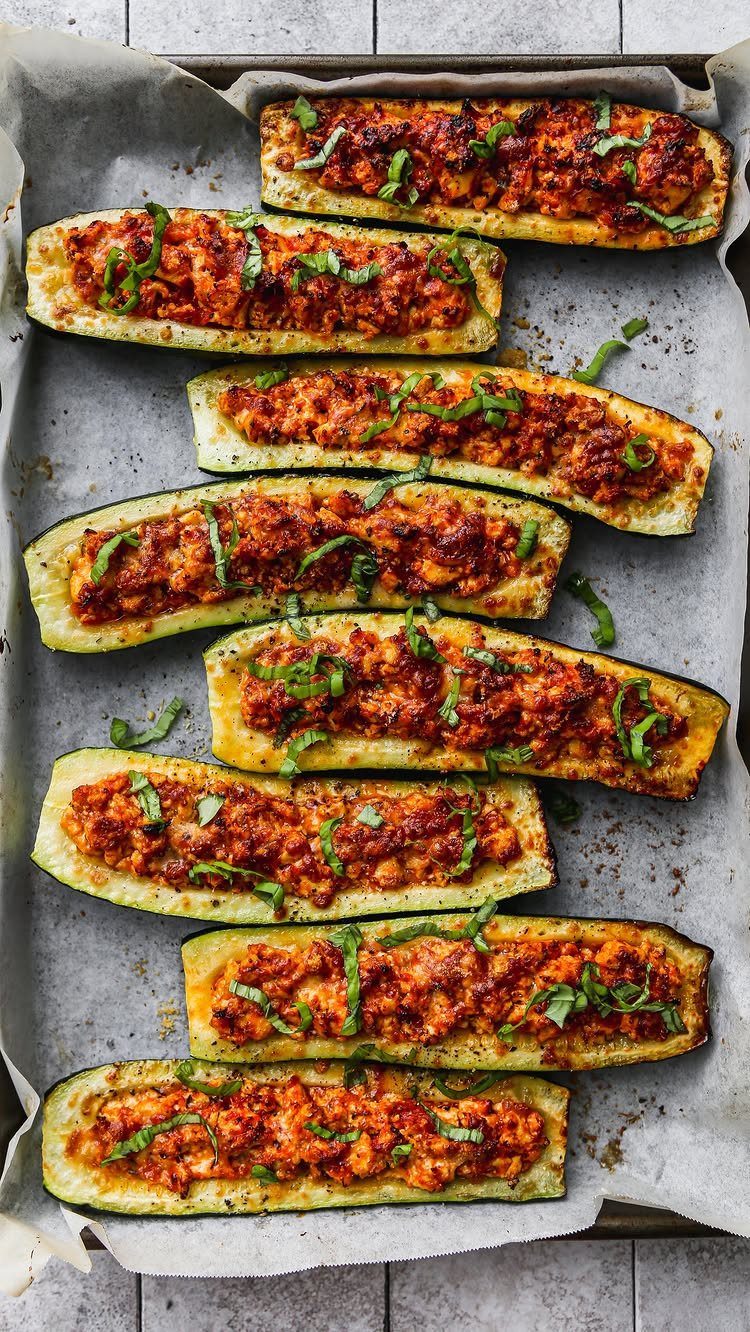 Stuffed zucchini boats filled with seasoned meat and herbs on a baking sheet.