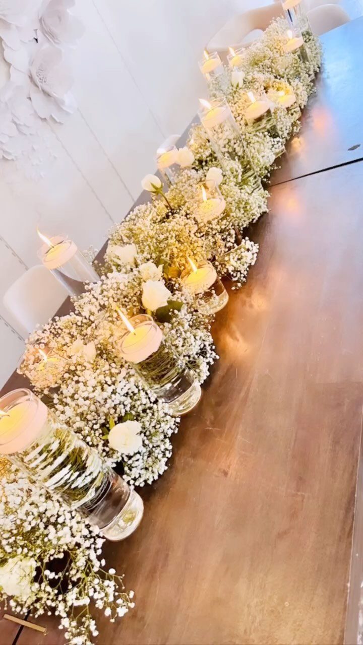 White baby's breath flower runner with lit floating candles on a wooden table