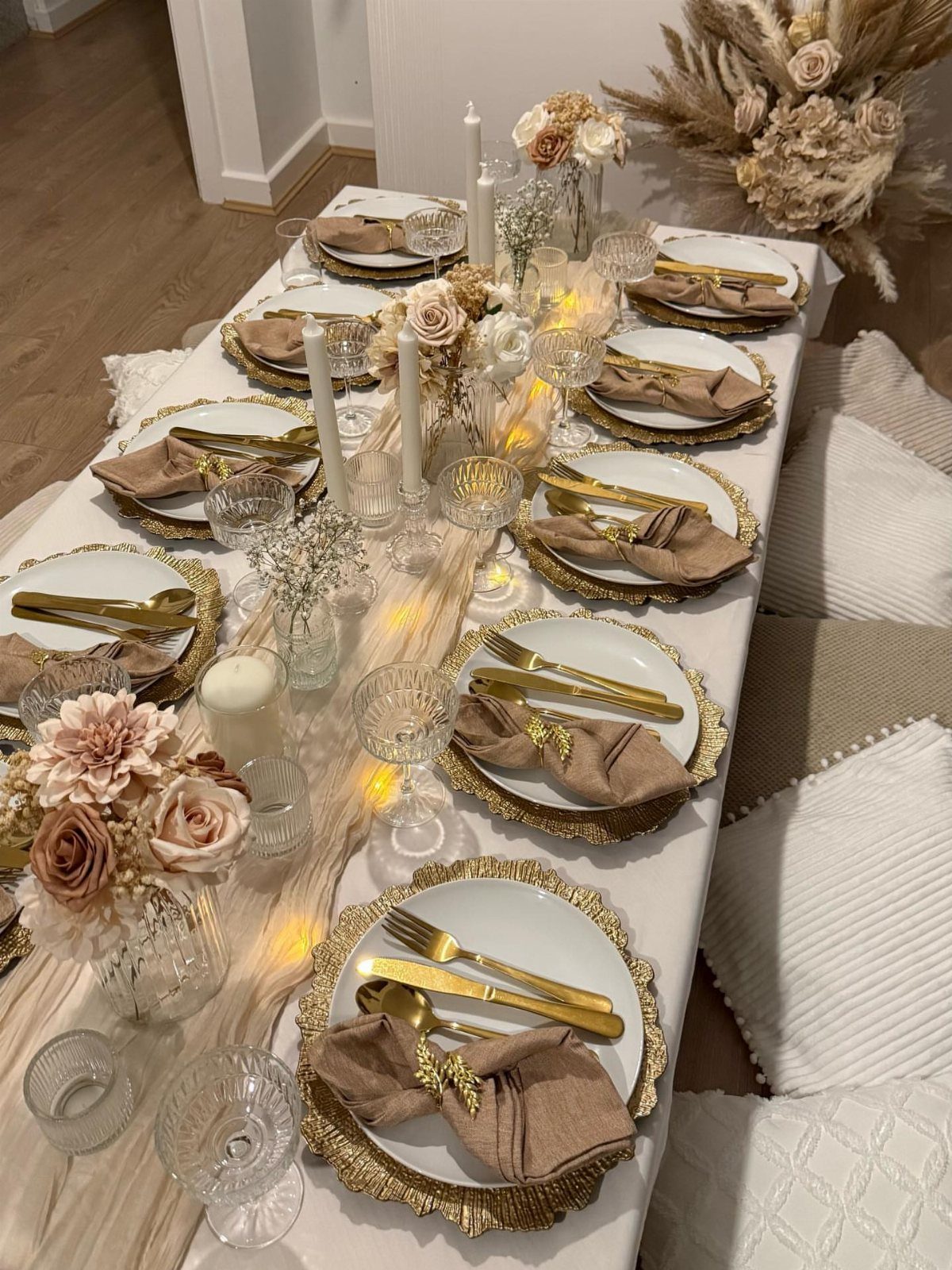 Elegant table setting with gold accents, white flowers, and warm fairy lights runner.