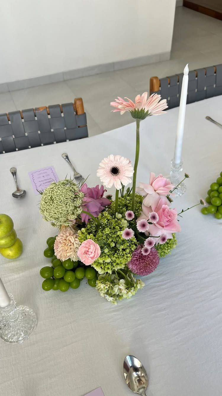 Floral centerpiece with pink and purple flowers and green grapes on white tablecloth