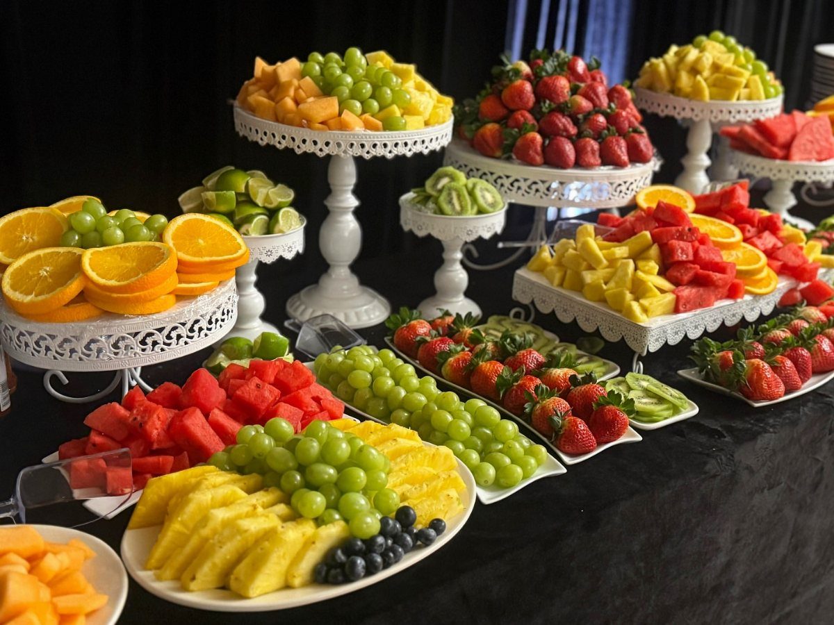 Assorted sliced fruits on white pedestals and platters arranged on a black table.