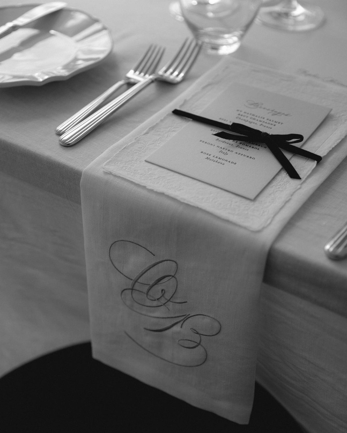 Monogrammed white fabric napkin with a menu card tied by a black ribbon.