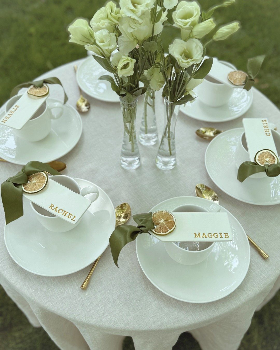 White teacups on a table with personalized place cards and dried citrus slices.