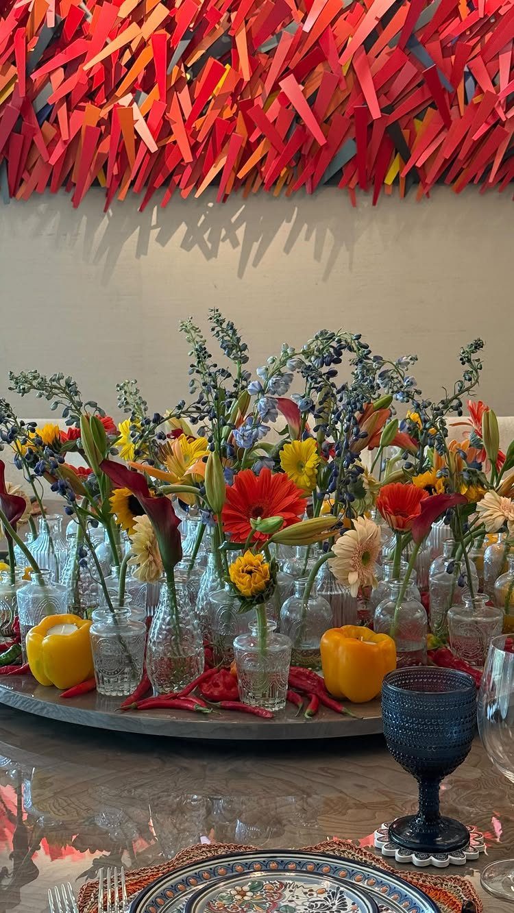 Multiple small glass vases with colorful flowers and peppers on a grey tray.