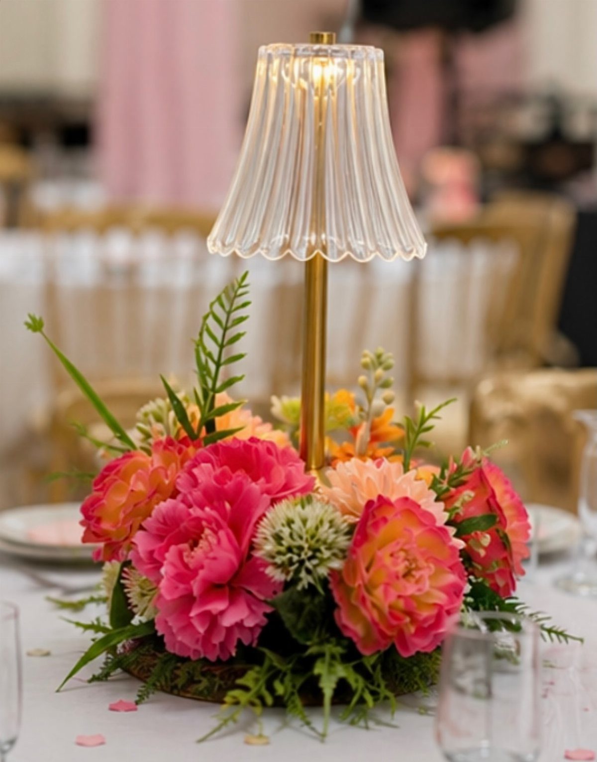 Floral centerpiece with pink peonies and a small gold lamp on a table