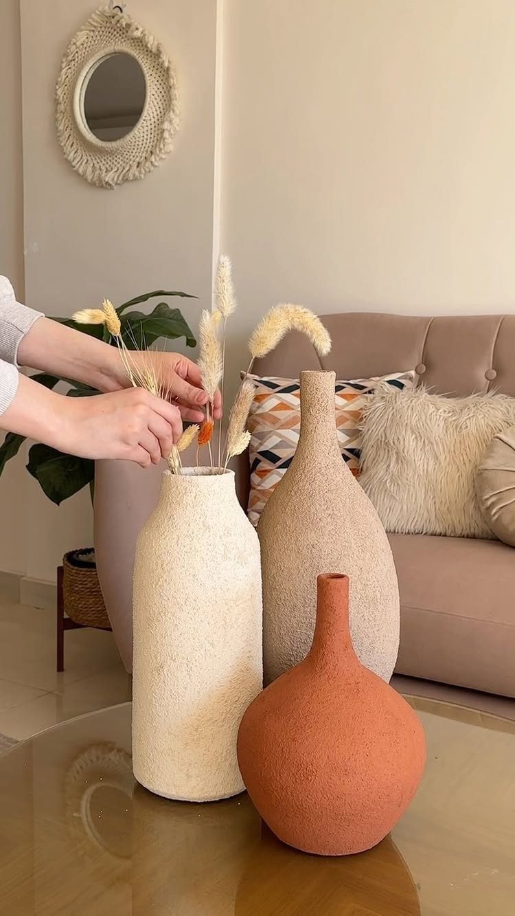 Three textured ceramic vases with dried grass on a glass coffee table.
