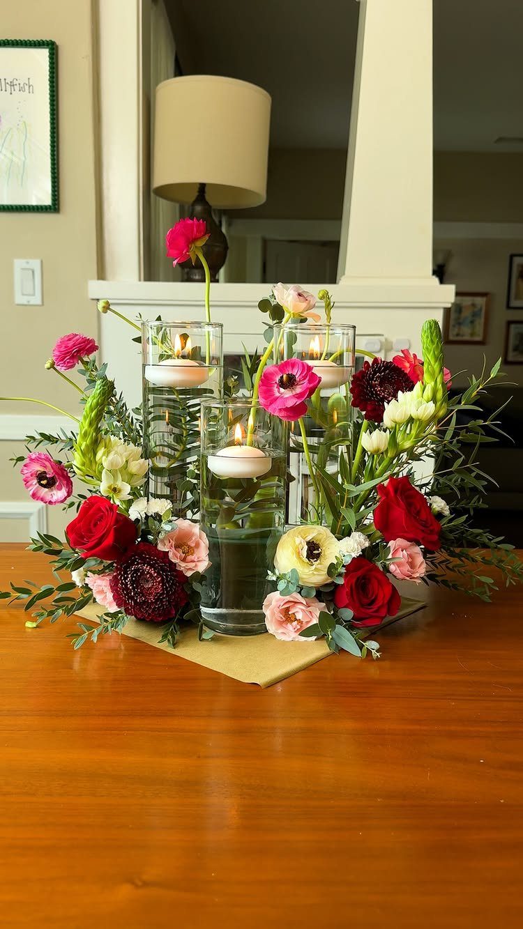 Floral arrangement with red and pink flowers surrounding three floating candle glass vases.